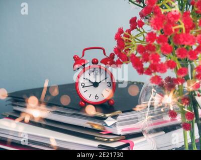 Alarm clock standing on table by stack of books against plain background Stock Photo