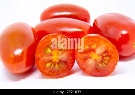 Baby plumb tomatoes isolated on a white background. One has been cut in half showing the seeds inside. Stock Photo