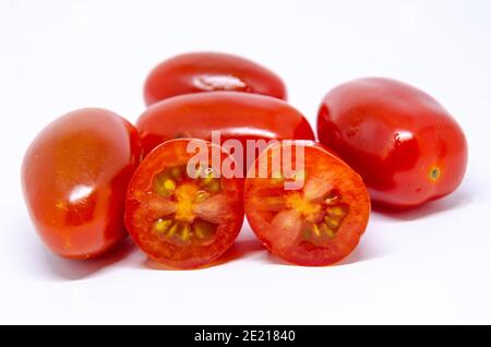 Baby plumb tomatoes isolated on a white background. One has been cut in half showing the seeds inside. Stock Photo