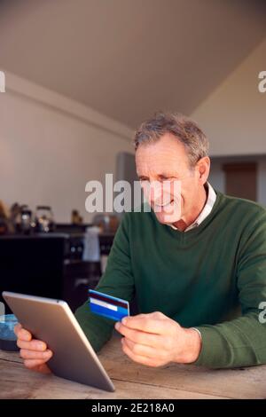 Senior Man At Home Buying Products Or Services Online Using Digital Tablet And Credit Card Stock Photo