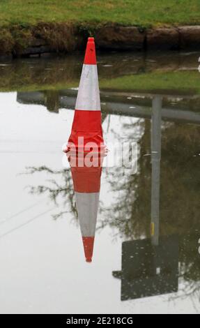 Cone on the ice, the freezing cold weather means water’s of the canal had frozen over and a traffic cone sits on the ice near a road over the canal Stock Photo