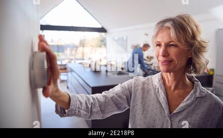 Mature Woman Adjusting Wall Mounted Digital Central Heating Thermostat Control At Home Stock Photo