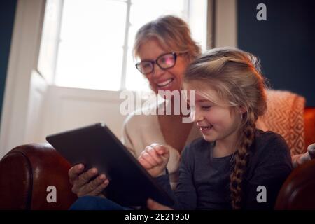 Granddaughter With Grandmother In Chair Looking At Digital Tablet At Home Together Stock Photo