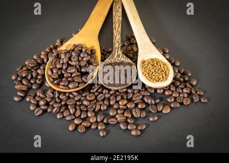 Coffee beans, coffee powder and instant coffee are placed in a wooden spoon placed on a black table top. Stock Photo