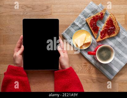Overhead Flat Lay Of Woman With Digital Tablet On Table Laid For Breakfast With Croissant And Coffee Stock Photo