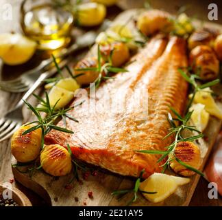 Baked salmon fillet with hasselback potatoes, lemon and fresh rosemary served on a wooden board close up view