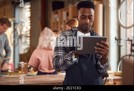 Male Craftsman In Carpentry Workshop For Bamboo Bicycles Using Digital Tablet Stock Photo