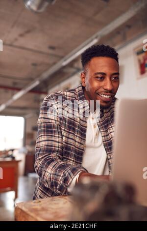 Male Carpenter In Workshop Doing Accounts On Laptop Stock Photo