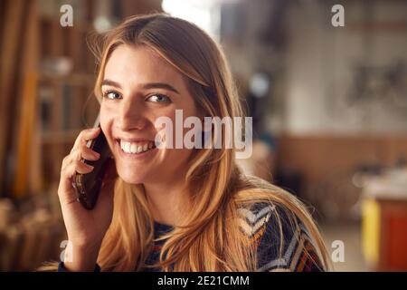 Portrait Of Female Business Owner In Workshop Making Call On Mobile Phone Stock Photo