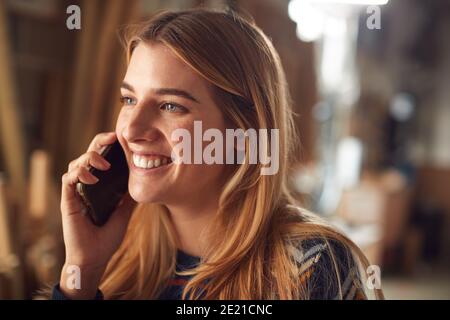 Female Business Owner In Workshop Making Call On Mobile Phone Stock Photo