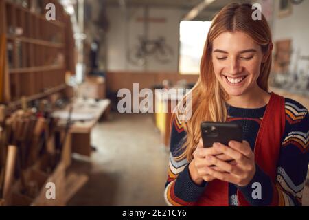 Female Business Owner In Workshop Using Mobile Phone Stock Photo