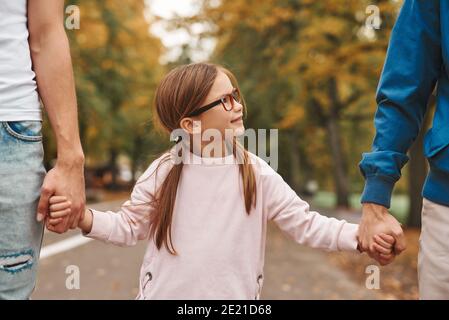 Cropped image of two gay parents with their adopted daughter holding hands and walking in park together. Happy LGBT family concept. Stock Photo