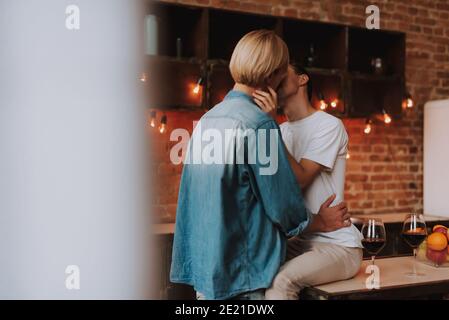 Loving gay couple at home. Two handsome men hugging and kissing on kitchen. LGBT concept. Stock Photo