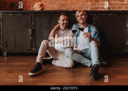 Loving gay couple at home. Two handsome men hugging, kissing and drinking wine on kitchen. LGBT concept. Stock Photo