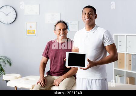 cheerful african american therapist holding digital tablet with blank screen near patient on blurred background Stock Photo