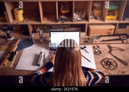 Female Business Owner Working Late In Carpentry Workshop Using Laptop Stock Photo