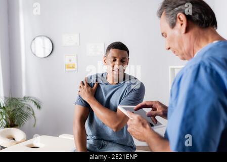african american patient suffering from pain near doctor using digital tablet Stock Photo