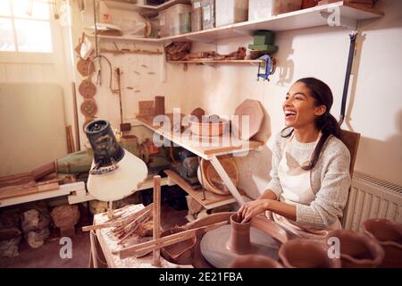 Female Potter Shaping Clay For Pot On Pottery Wheel In Ceramics Studio Stock Photo
