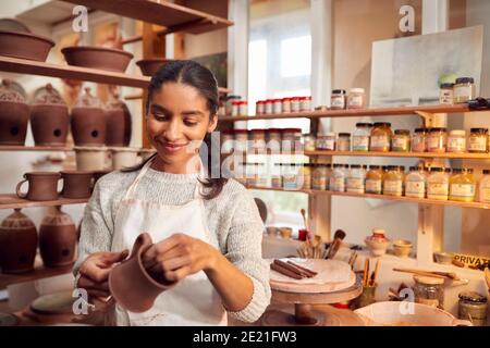 Female Potter Fitting Clay Handles To Mugs In Ceramics Studio Stock Photo