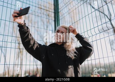 Waist up of smiling beautiful woman holding smartphone while making photo with metal grid on the background Stock Photo