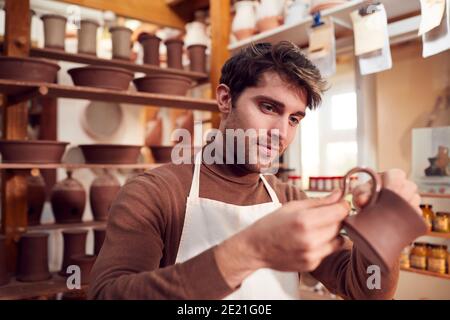 Male Potter Fitting Clay Handles To Mugs In Ceramics Studio Stock Photo