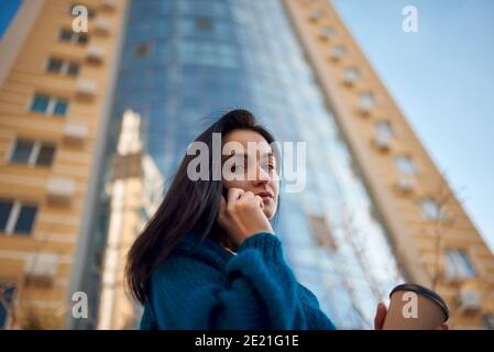 Low angle view of a young adorable lady walking near modern multistoreyed building while talking on mobile phone Stock Photo