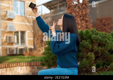 Side view of a pretty female student taking self picture outdoors with a small fluffy conifer on background Stock Photo