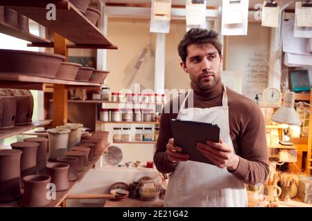 Male Potter In Ceramics Studio Checking Orders Using Digital Tablet Stock Photo