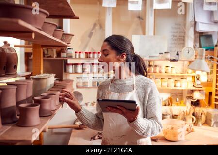 Female Potter In Ceramics Studio Checking Orders Using Digital Tablet Stock Photo