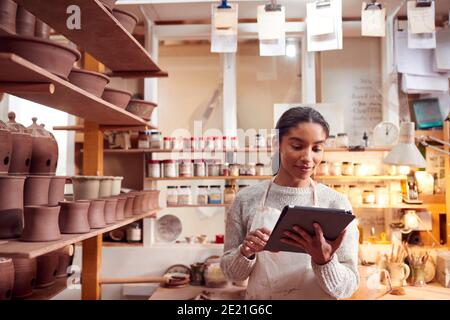 Female Potter In Ceramics Studio Checking Orders Using Digital Tablet Stock Photo