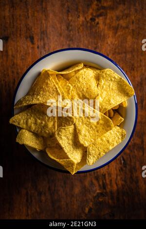 Salted tortilla chips. Yellow nachos triangle in bowl on wooden table. Top view. Stock Photo