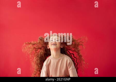 Portrait Of Girl With Long Red Hair Jumping In Air Against Red Studio Background Smiling At Camera Stock Photo