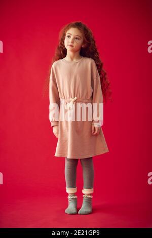 Full Length Portrait Of Girl With Long Red Hair Against Red Studio Background Stock Photo