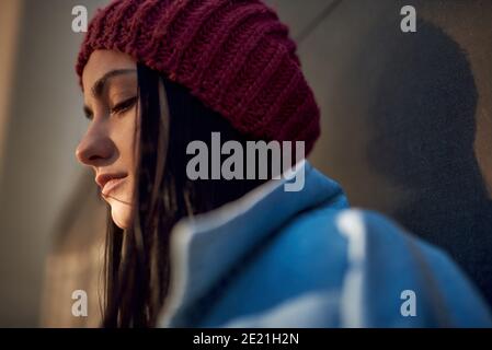 Low angle portrait of an unhappy brunette lady in denim jacket with long straight hair and stylish woolen beanie Stock Photo
