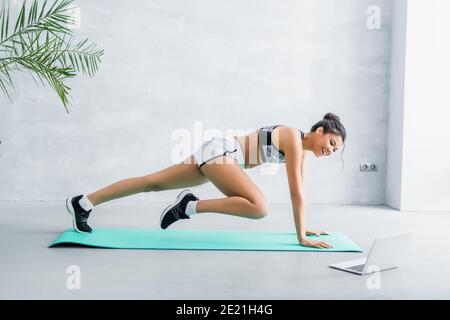 side view of happy african american sportswoman practicing one legged plank pose near laptop Stock Photo