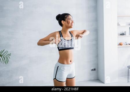 happy african american woman in sportswear warming up arms at home Stock Photo