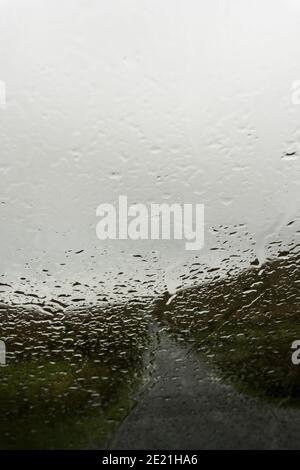 Looking through a car window blurred by raindrops. As a road crosses a bleak moorland valley. On a moody, misty day. Wales, UK. Stock Photo