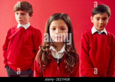 Group Of Elementary School Pupils Wearing Uniform Against Red Studio Background Stock Photo