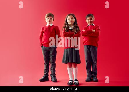Group Of Elementary School Pupils Wearing Uniform Folding Arms Against Red Studio Background Stock Photo