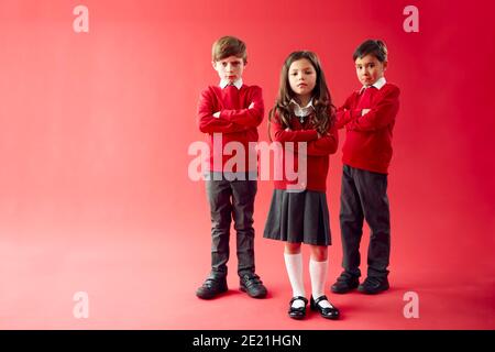 Group Of Elementary School Pupils Wearing Uniform Folding Arms Against Red Studio Background Stock Photo