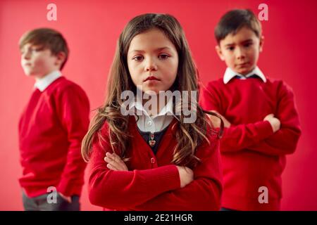 Group Of Elementary School Pupils Wearing Uniform Folding Arms Against Red Studio Background Stock Photo