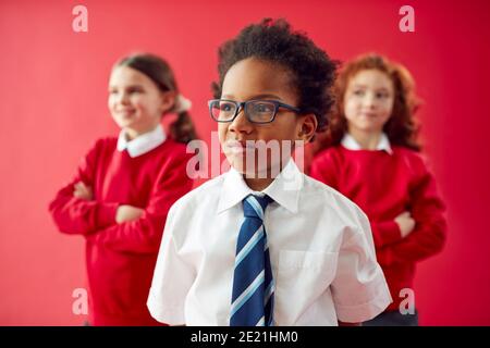 Group Of Elementary School Pupils Wearing Uniform Folding Arms Against Red Studio Background Stock Photo