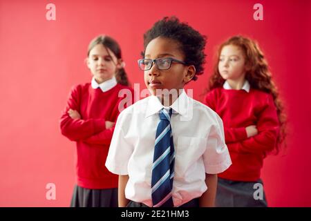 Group Of Elementary School Pupils Wearing Uniform Folding Arms Against Red Studio Background Stock Photo