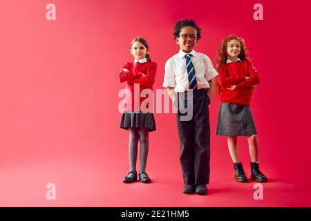 Group Of Elementary School Pupils Wearing Uniform Folding Arms Against Red Studio Background Stock Photo