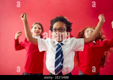 Group Of Excited Elementary School Pupils Wearing Uniform Having Fun Against Red Studio Background Stock Photo