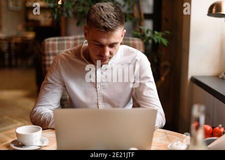 Portrait of young Caucasian man in casual shirt using laptop computer at cafe while having lunch. Lifestyle concept Stock Photo