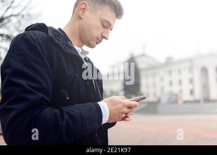 Side view of handsome guy walking while using mobule phone outdoors. Copy space. Lifestyle concept Stock Photo