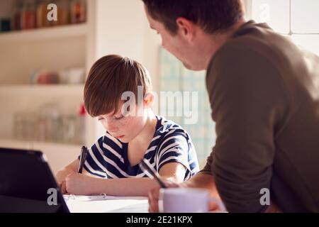 Father Helping Son With Homework Sitting At Kitchen Counter Using Digital Tablet Together Stock Photo