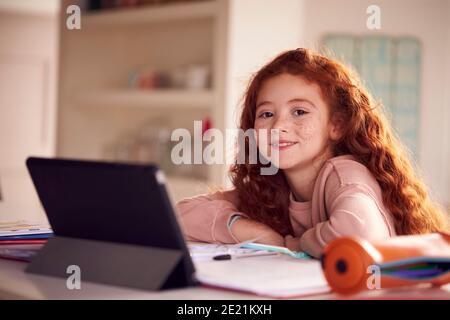 Portrait Of Girl Sitting At Kitchen Counter Doing Homework Using Digital Tablet Stock Photo