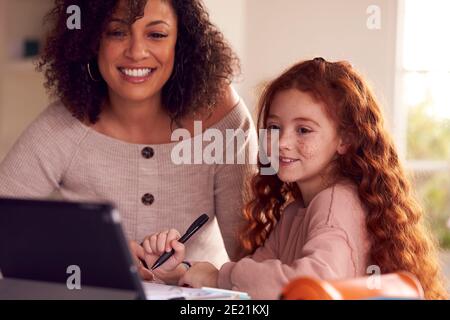 Mother Helping Daughter With Homework Sitting At Kitchen Counter Using Digital Tablet Together Stock Photo
